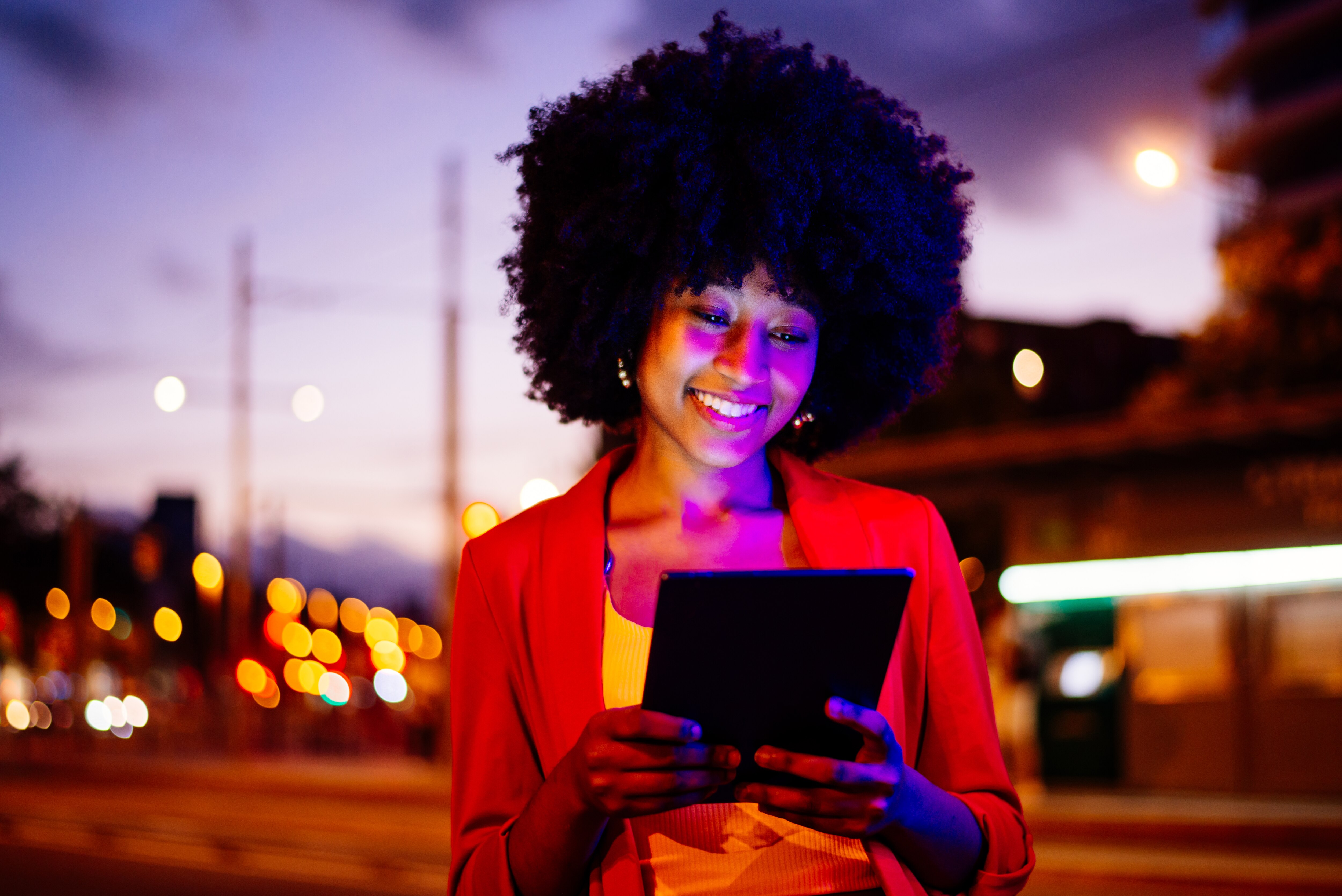 Silhouette of a woman at twilight standing in front of a skyscraper window using cloud computing services on her laptop